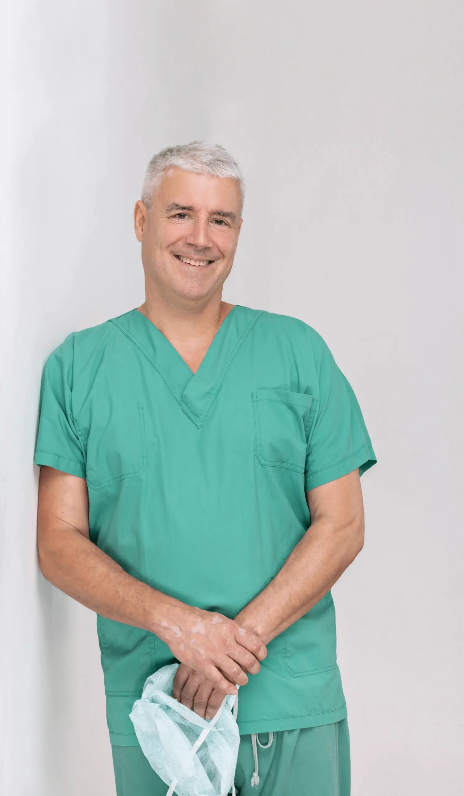 Dr Straka lehnt in einem grünen Krankenhaus Gewand an der Wand Scaled