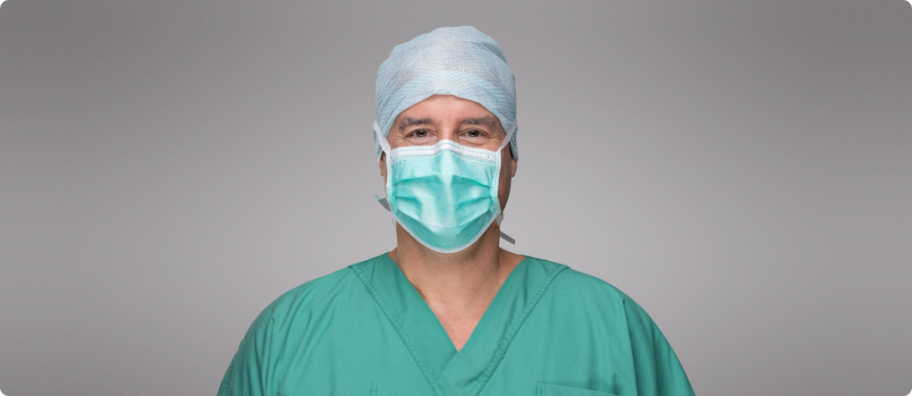 Dr Straka mit medizinischer Maske und Haarschutz im Portrait Bild